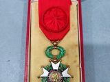 une image représentant une boîte rouge contenant une médaille d'or et un ruban rouge
