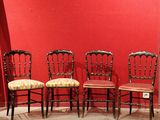 four antique chairs are lined up against a red wall