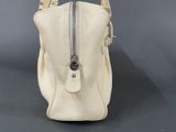 white leather handbag with zippers and metal handles on a gray surface