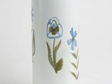 un vase blanc orné de fleurs bleues, posé sur un fond blanc