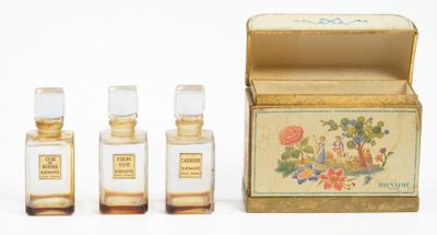 trois petits flacons de parfum posés à côté d'une boîte sur une surface blanche