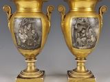 deux vases en or ornés de représentations de personnes, posés sur des socles