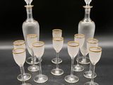 six clear wine glasses and a decanter with gold rims