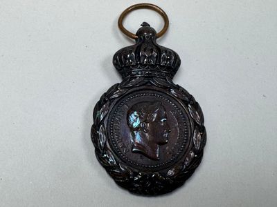 une vieille médaille en bronze ornée d'une couronne, posée sur un fond blanc