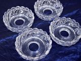 four clear glass candle holders sitting on a blue velvet surface