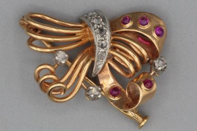 une photo d'une broche en forme de papillon, en or et diamants, posée sur une surface grise