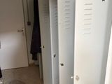 Plusieurs casiers sont alignés dans une pièce, et une personne se tient dans l'embrasure de la porte.