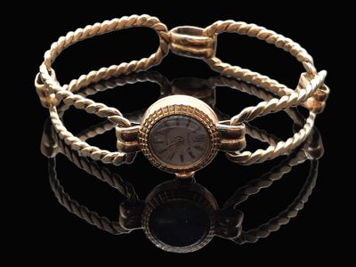 une photo d'un bracelet en or avec une montre, sur un fond noir