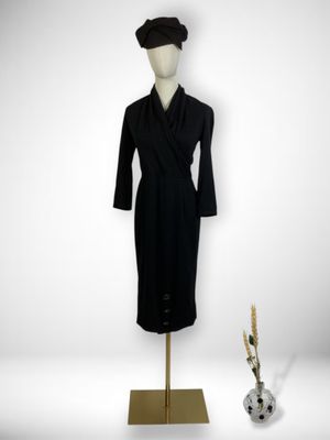 black dress and hat on a mannequin stand next to a vase of flowers