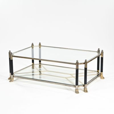 une table basse en verre et laiton avec deux pieds noirs