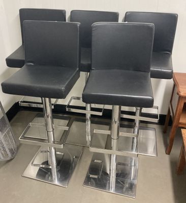 trois tabourets de bar en cuir noir posés sur un sol métallique