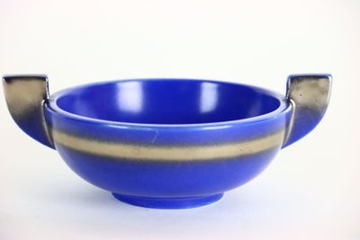 un bol bleu muni d'une poignée en métal, posé sur une surface blanche