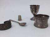 a silver cup, spoon, and a thimble on a table