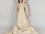 une poupée ancienne représentant une femme vêtue d'une robe blanche et d'un bonnet
