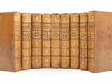 six old books are lined up in a row on a white surface