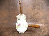 a small white vase with a wooden handle on a brown surface