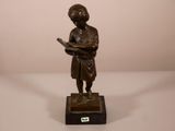 statue en bronze représentant un garçon en train de lire un livre, posée sur un socle en marbre