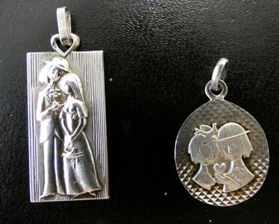 two silver pendants of a woman and a child on a black surface