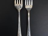 two forks are sitting next to each other on a black surface