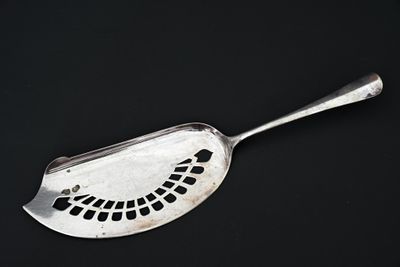 une cuillère en argent percée de trous, posée sur une surface noire