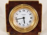 une petite horloge avec des chiffres romains posée sur une table