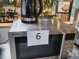 a silver microwave with a black kettle on top of it