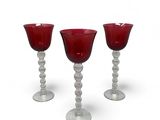 three red wine glasses sitting on top of each other on a white surface
