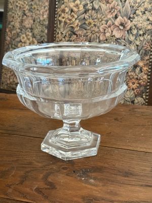 a glass bowl on a wooden table with a floral wallpaper behind it
