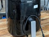 une friteuse à air chaud Philips posée sur une table en bois, avec une boîte de nourriture en arrière-plan