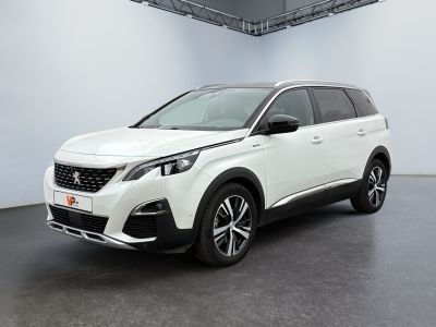 Une voiture blanche est garée dans une pièce blanche au sol noir.