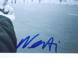 signed photograph of a person pointing at a beach with people walking on the beach in the background