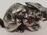 a silver rabbit figurine sitting on a white surface