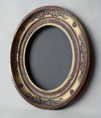 an oval mirror with a gold frame on a gray wall