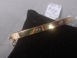 gold plated bracelet with multi colored stones on it on a pillow
