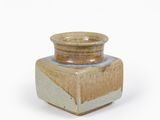 un petit vase marron et blanc posé sur une surface blanche