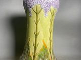 a green vase with purple flowers on it sitting on a table