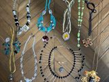 Plusieurs colliers et boucles d'oreilles sont disposés sur un parquet.