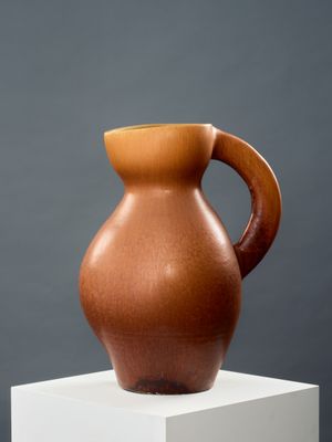 un vase marron posé sur un socle blanc, devant un mur gris