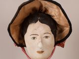 a wooden head of a woman wearing a hat and a pink scarf