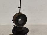 une photo représentant une lampe noire posée sur un pied, sur un sol blanc