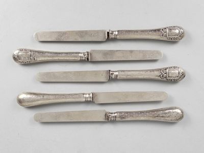 six silverplated knives with ornate designs on them on a white surface