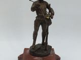 statue en bronze représentant un homme tenant un fusil, posée sur un socle en bois