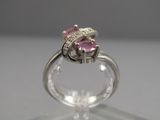 un gros plan d'une bague sertie d'un diamant rose posée sur une surface transparente