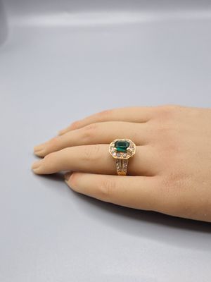 a woman ' s hand holding a ring with a green stone on it