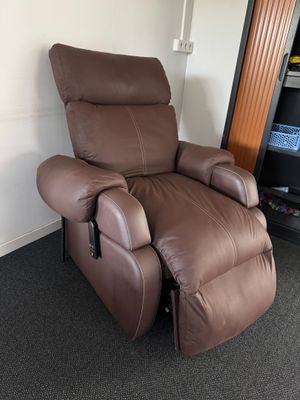 un fauteuil inclinable marron dans une pièce où se trouve une bibliothèque