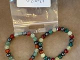 deux bracelets composés de perles vertes, rouges et noires, dans un sachet