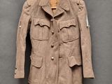 Une veste marron est suspendue à un cintre accroché à un mur gris.