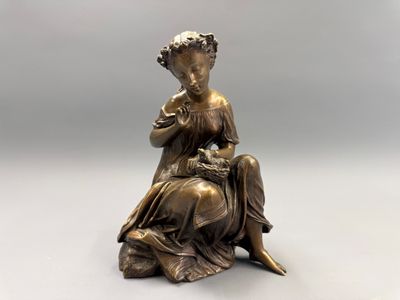 une statue en bronze représentant une femme assise sur un rocher, une fleur à la main