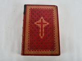 an old red book with a cross on it sitting on a white surface