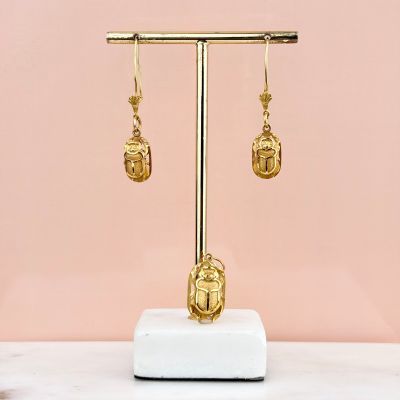 a pair of gold earrings on a stand against a pink wall